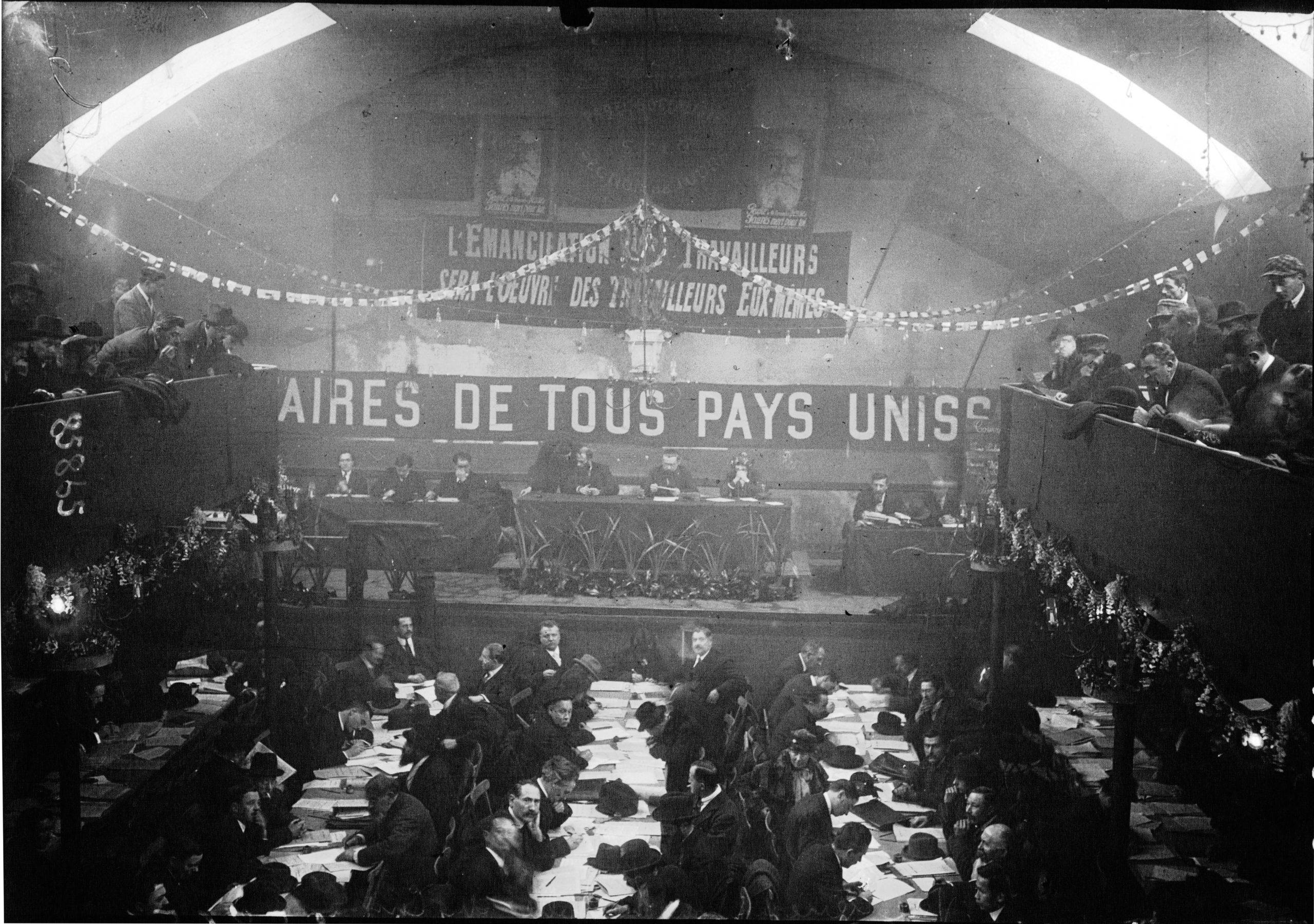 Vue générale de la salle au Congrès de Tours avec en arrière-plan la grande banderole « Prolétaires de tous les pays, unissez-vous ! », et deux portraits de Jean Jaurès