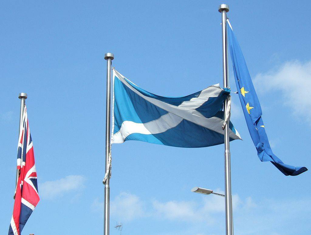 Le drapeau écossais entre celui du Royaue Uni et celui de l'Union européenne devant le parlement à Edimbourg.  Source : Wikipédia.