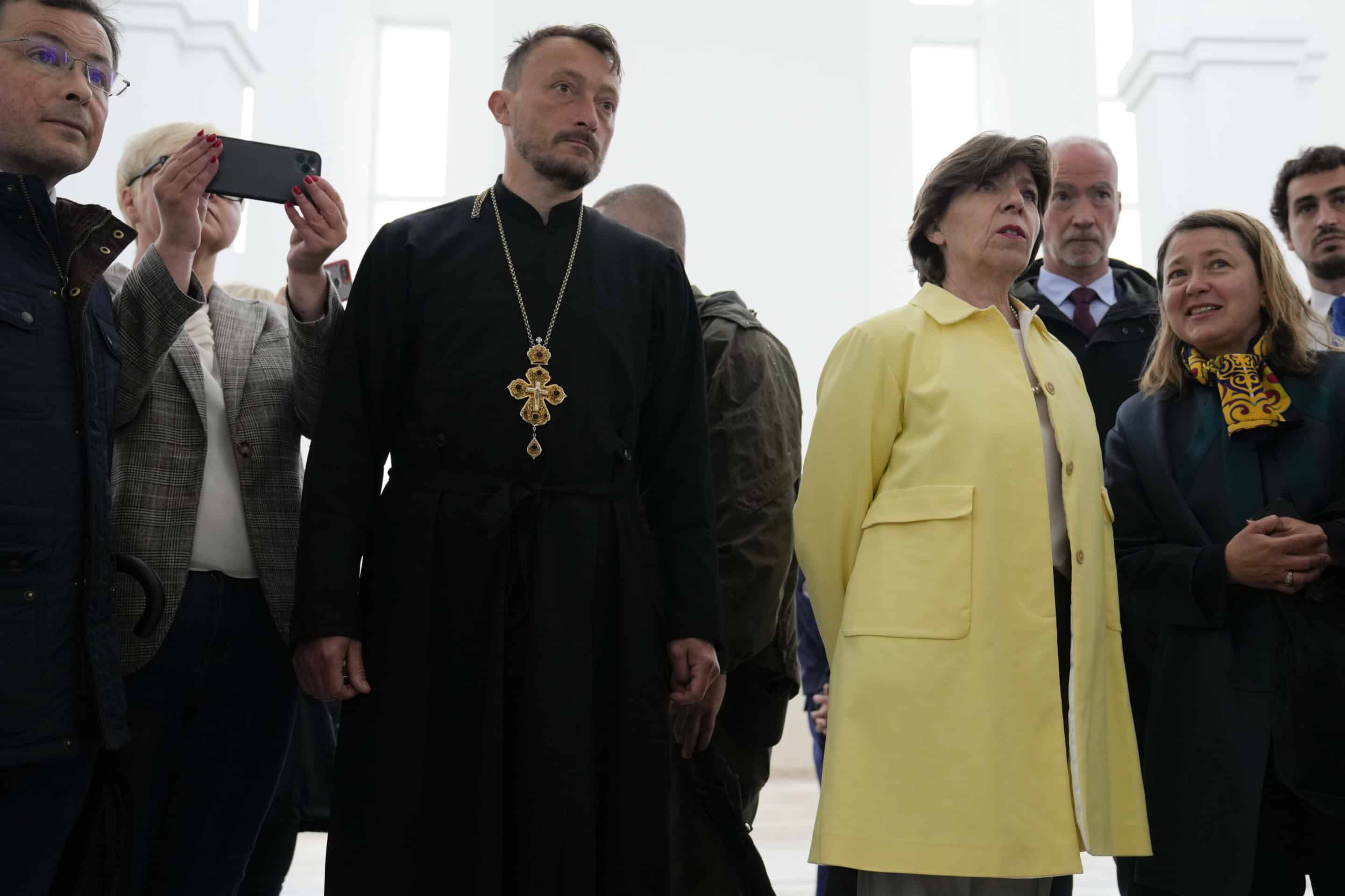 La ministre française des Affaires étrangères, Catherine Colonna, deuxième à droite, regarde des photos montrant les corps de civils tués pendant l'occupation russe lors d'une visite à l'église de Bucha, dans la banlieue de Kiev, en Ukraine, lundi 30 mai 2022. 
Crédits : AP Photo/Natacha Pisarenko